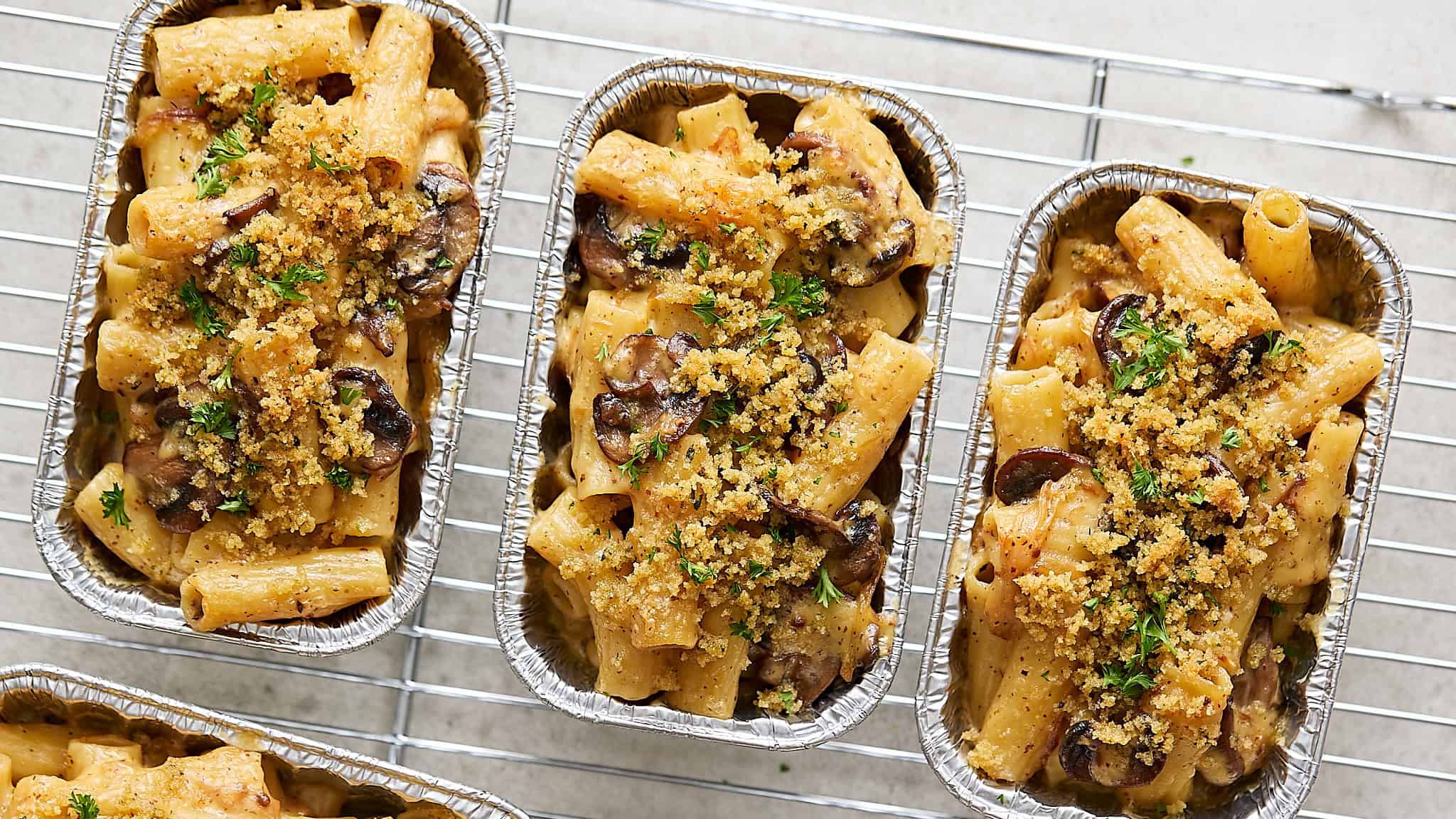Creamy mushroom and chicken baked pasta in individual aluminum foil containers garnished with fresh parsley. Delicious comfort food perfect for easy weeknight dinners.