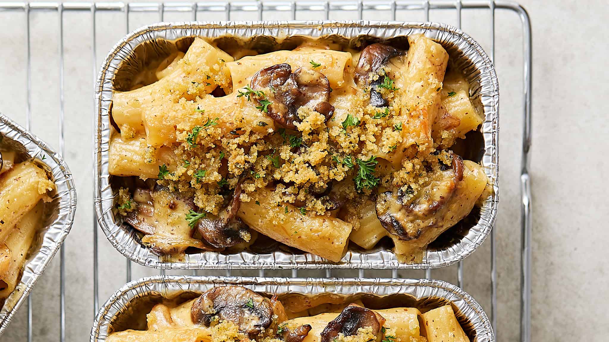 Creamy mushroom and chicken pasta casserole topped with toasted breadcrumbs and fresh herbs, served in aluminum baking dishes for a comforting, hearty meal.