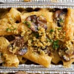 Creamy mushroom and chicken pasta bake in aluminum foil containers with breadcrumb topping, garnished with fresh parsley. Perfect for homemade comfort food, easy dinner recipes, and family meals.