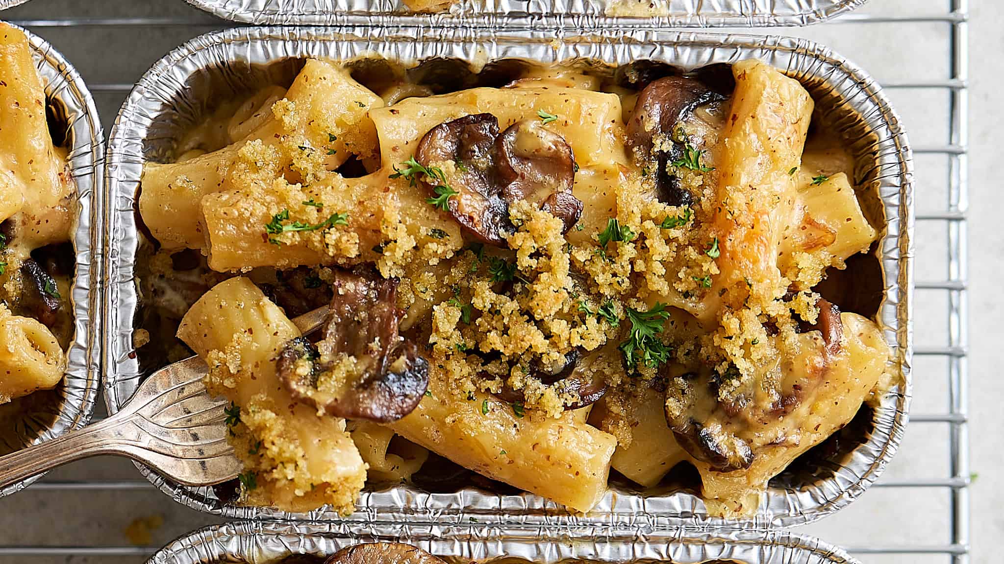 Creamy mushroom and chicken pasta bake in aluminum foil containers with breadcrumb topping, garnished with fresh parsley. Perfect for homemade comfort food, easy dinner recipes, and family meals.