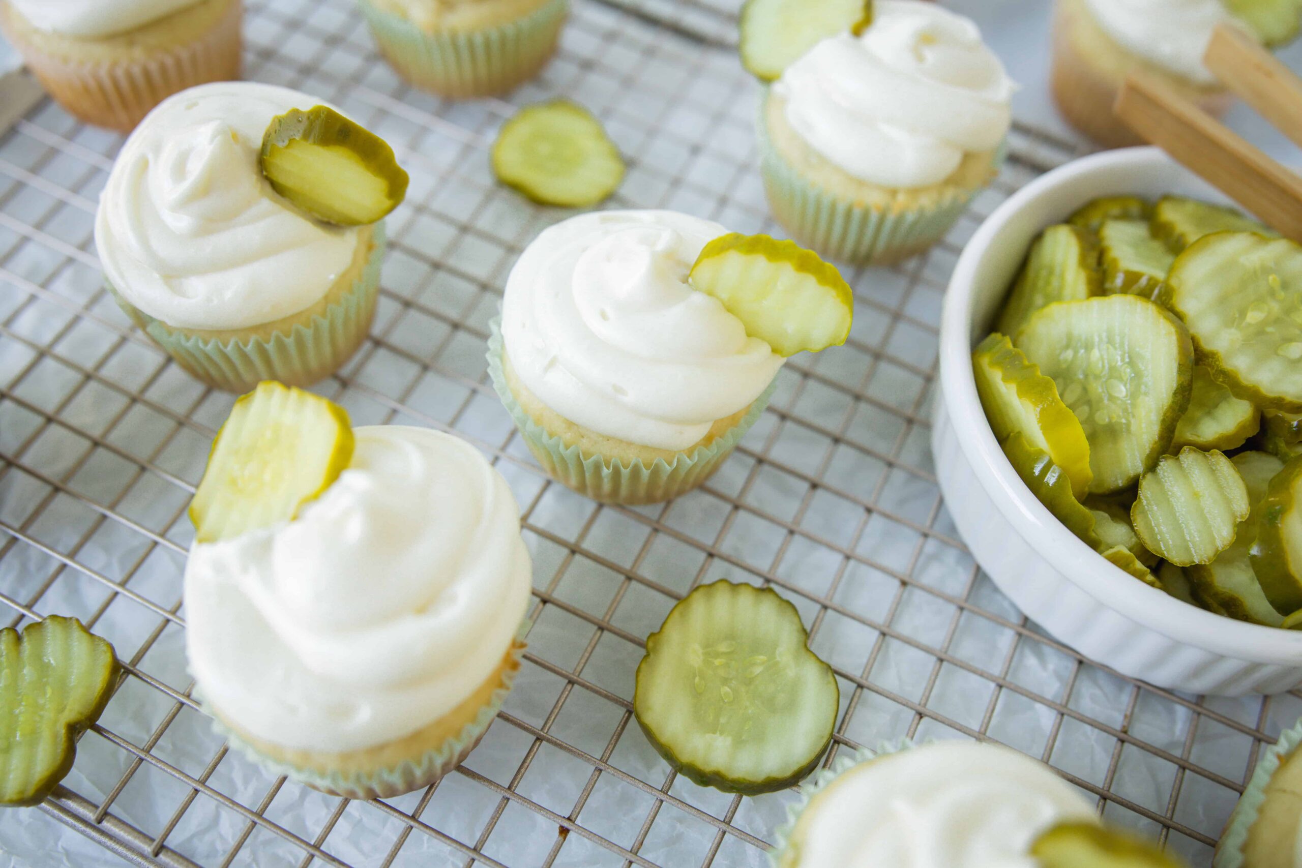 Fresh cucumber and cream cheese cupcakes garnished with cucumber slices on a cooling rack. Perfect for summer snacks or party treats.