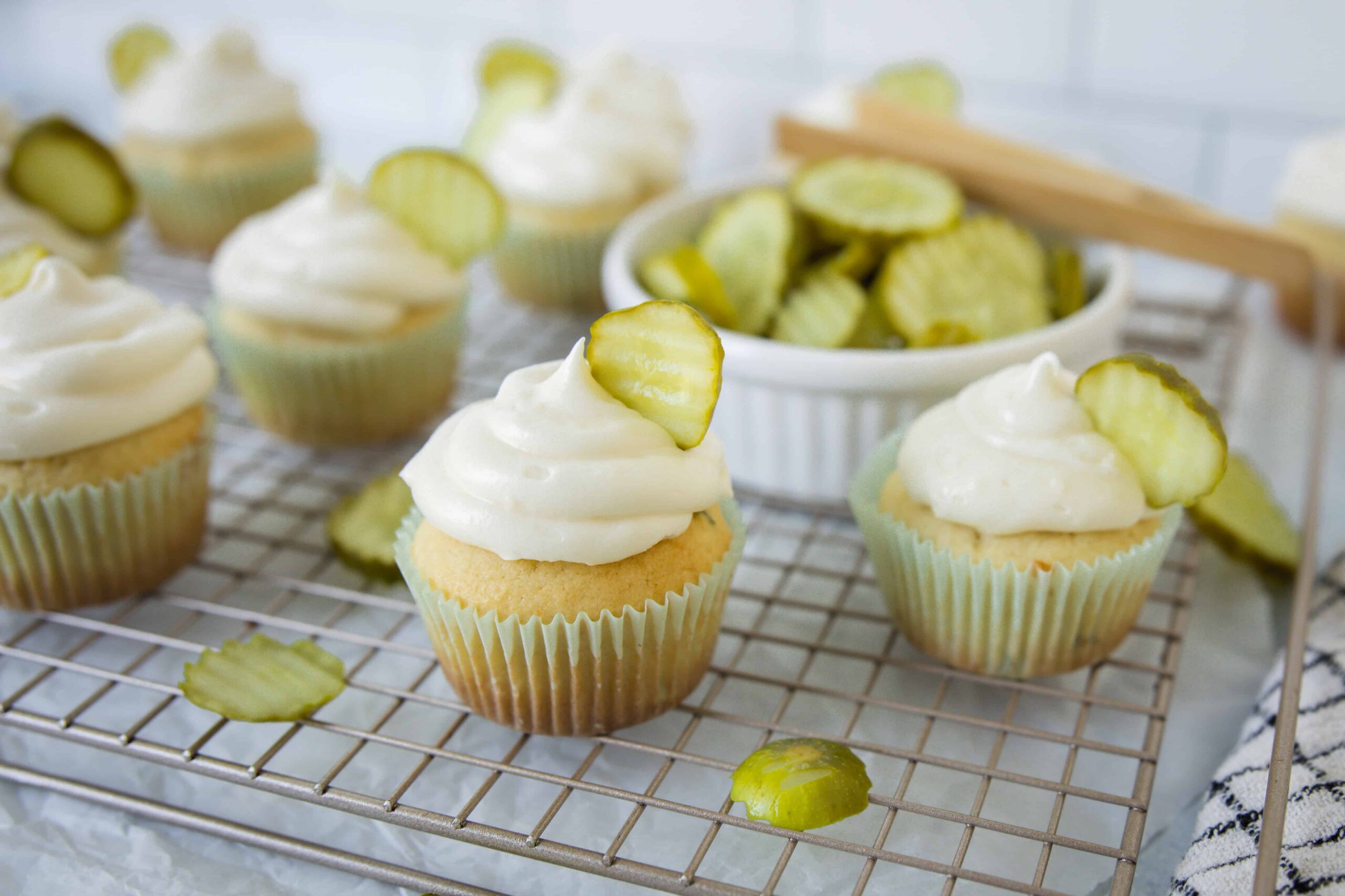Sweet cucumber cupcakes with creamy frosting and pickle slices, perfect for snack or party treats, showcased on a cooling rack with scattered cucumber slices.