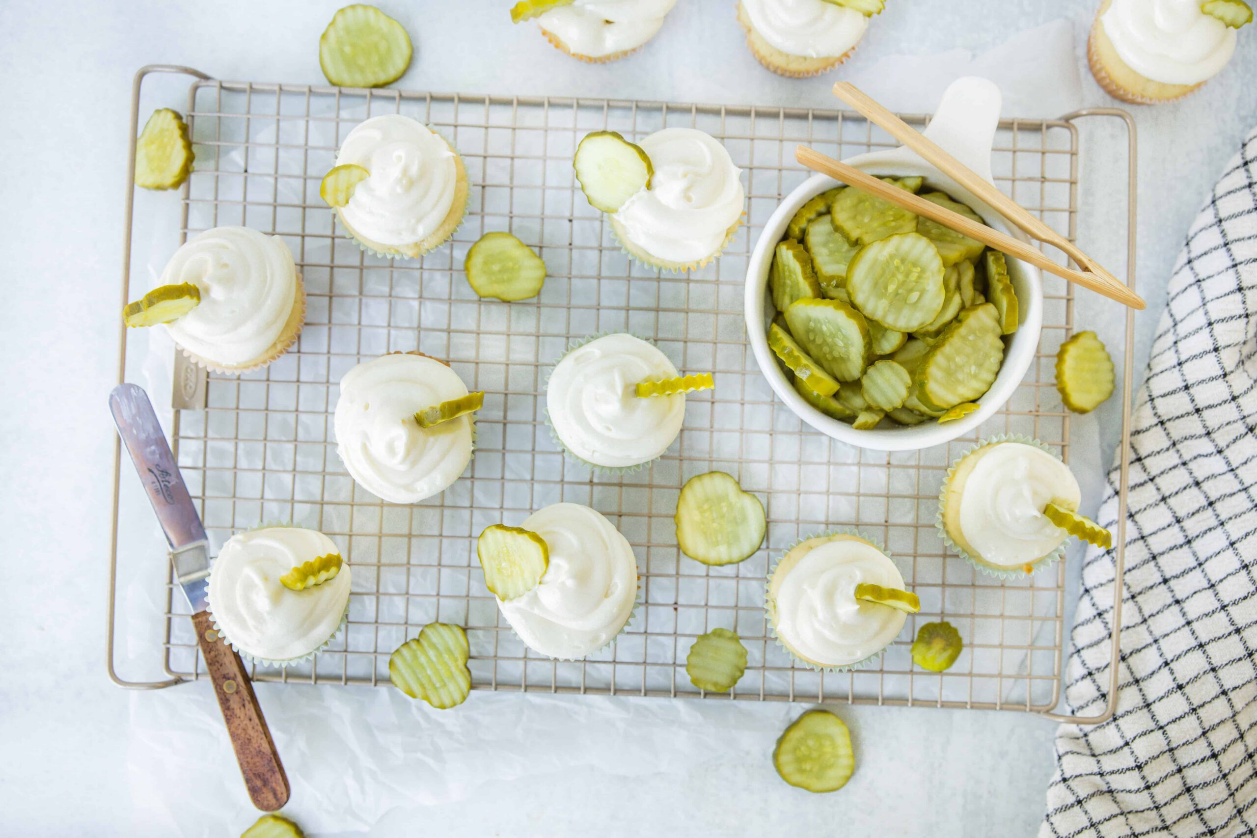 Fresh homemade pickles on a cooling rack with cream cheese and pickle slices, featuring a white and light green color scheme for a tasty snack or appetizer.