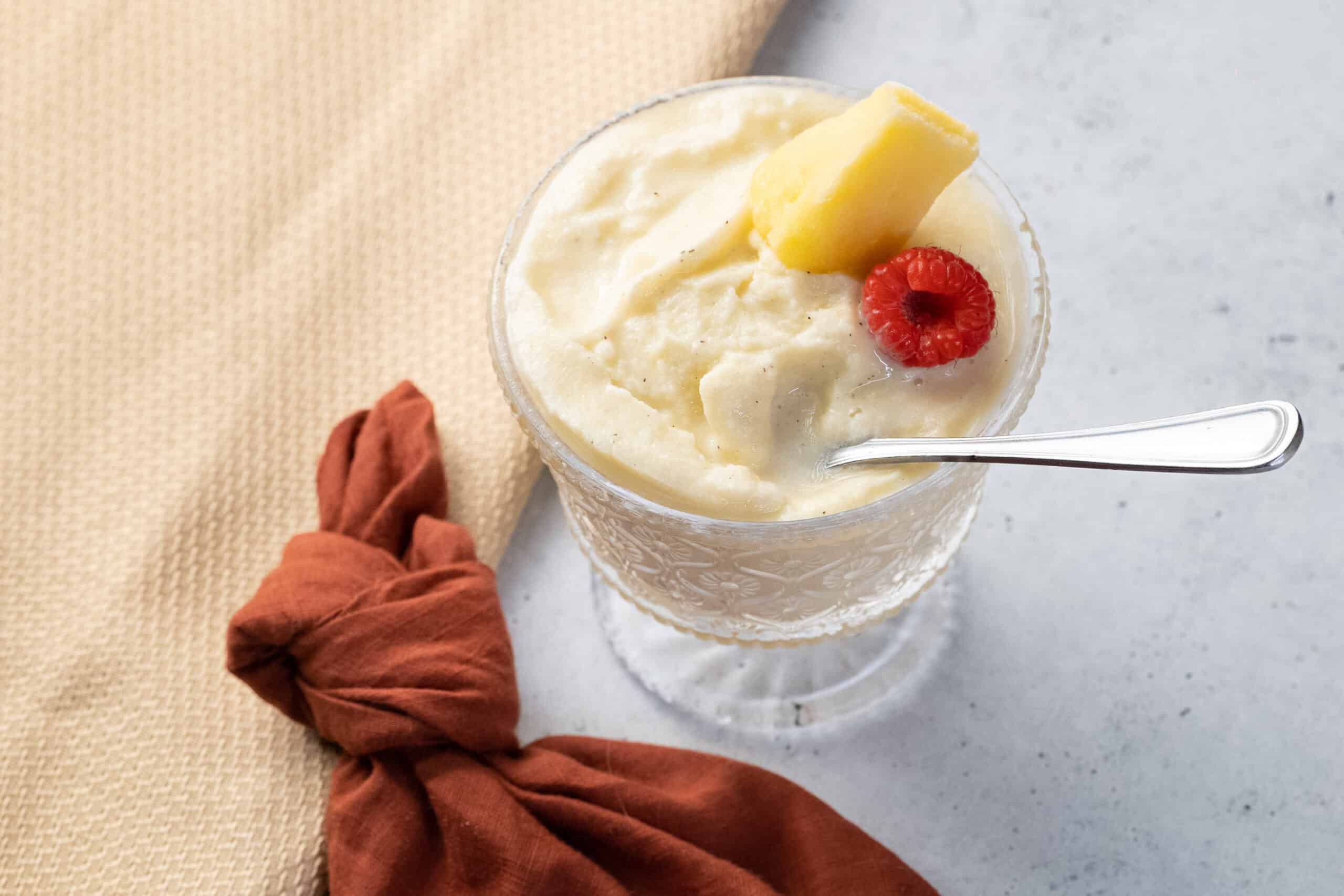 Creamy vanilla ice cream topped with fresh raspberry and pineapple chunks in a decorative glass. Perfect for summer desserts or refreshing treats.