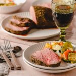 Juicy, perfectly cooked prime rib with seasoned crust served with fresh vegetable medley and a glass of red wine, set on a rustic table for a hearty dinner.