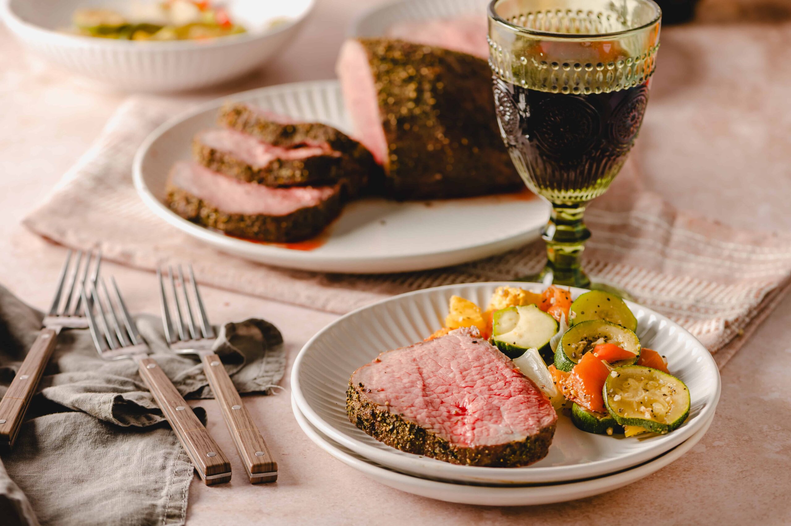 Juicy, perfectly cooked prime rib with seasoned crust served with fresh vegetable medley and a glass of red wine, set on a rustic table for a hearty dinner.