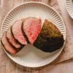 Juicy, perfectly cooked beef tenderloin roast with a flavorful herb crust, sliced and served on a white ceramic plate, ideal for gourmet dinners and special occasions.