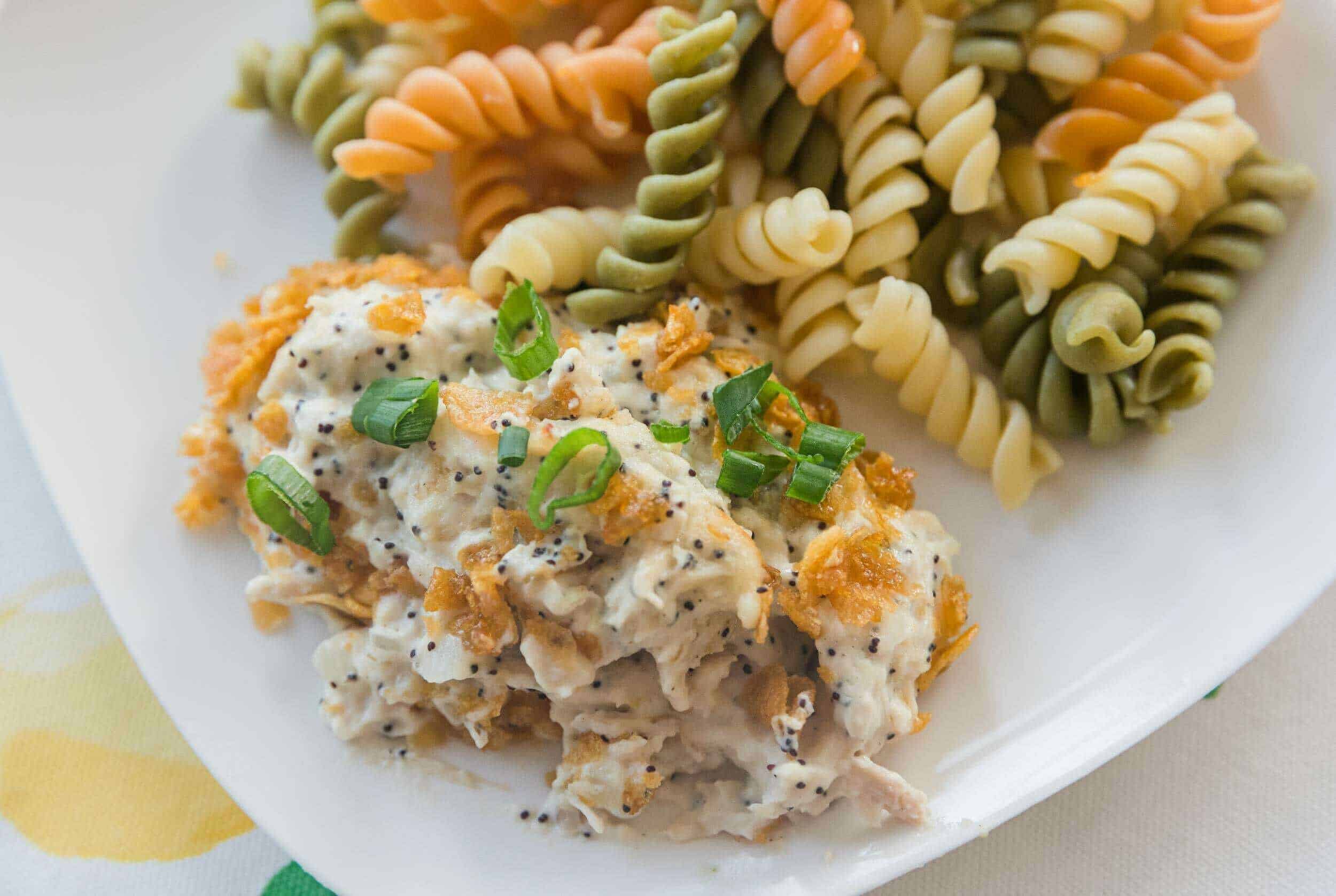 Creamy chicken salad with poppy seeds and green onions served with colorful tri-color rotini pasta on a white plate. Perfect for a delicious lunch or dinner, easy to prepare.