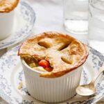 Golden-brown vegetable pot pie served in a ramekin on vintage blue and white patterned dishware with glasses of water in the background.