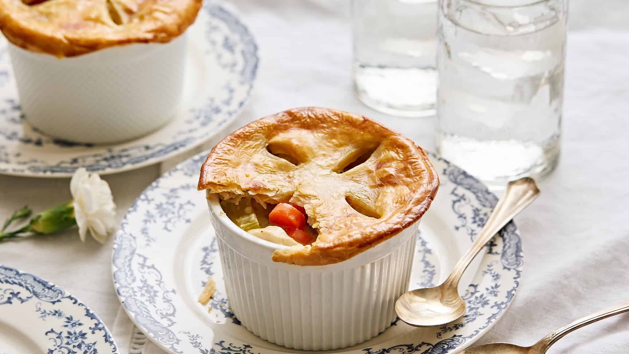 Golden-brown vegetable pot pie served in a ramekin on vintage blue and white patterned dishware with glasses of water in the background.