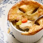 Creamy chicken pot pie with golden flaky crust, served in a white ramekin on a blue and white patterned plate. Comes with tender chicken, carrots, and celery in a savory broth. Perfect comfort food.