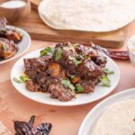 Tender, flavorful beef rendang cooked in rich spices, served with fresh cilantro, alongside rice and traditional flatbread, perfect for an authentic Indonesian meal.