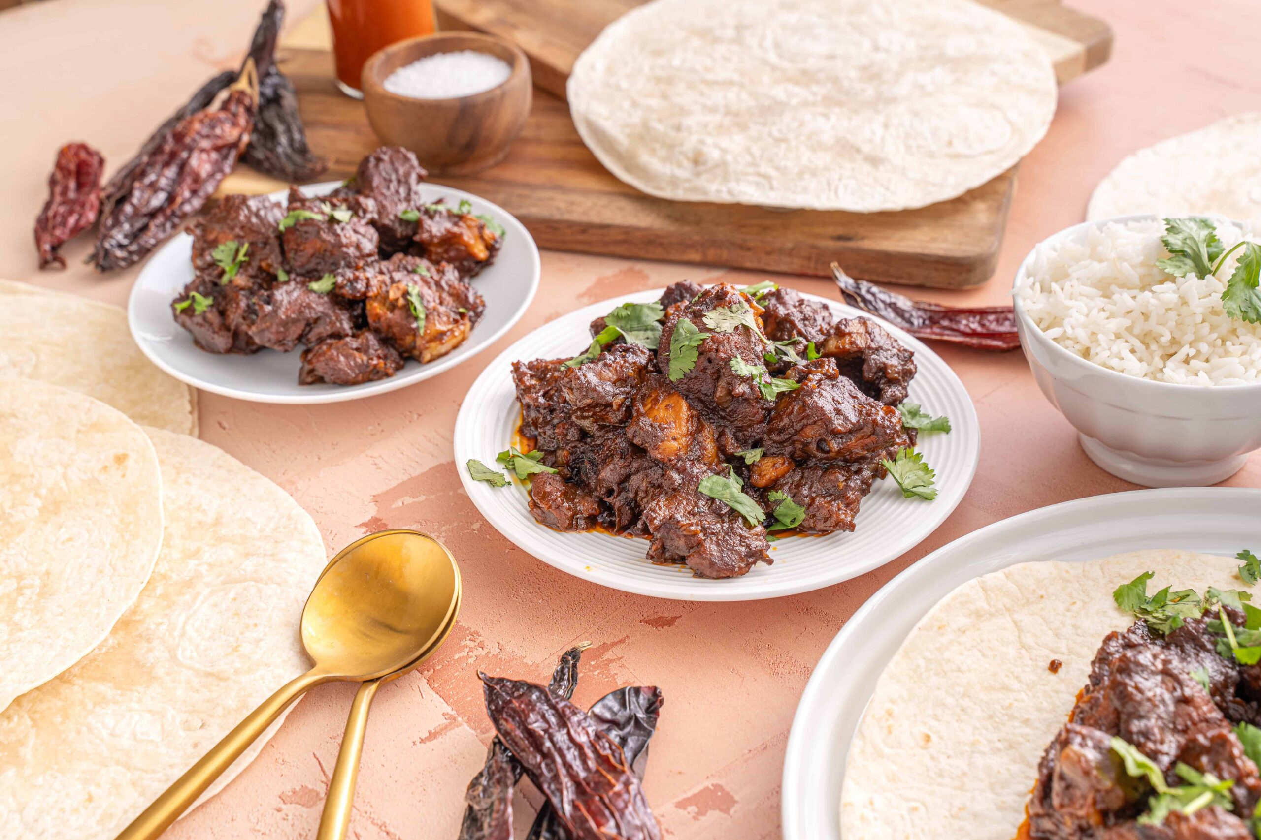 Savory Mexican-style beef and pork stew served with warm tortillas, rice, and dried chili peppers, showcasing traditional ingredients and flavors for authentic Mexican cuisine.