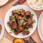 Succulent plate of spicy beef ribs garnished with fresh cilantro, served alongside fluffy white rice and soft tortillas for a delicious Mexican-inspired meal.