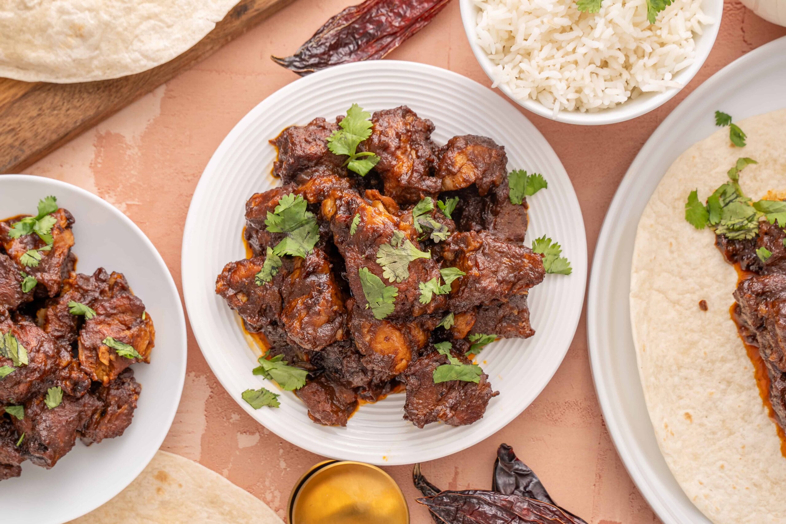 Succulent plate of spicy beef ribs garnished with fresh cilantro, served alongside fluffy white rice and soft tortillas for a delicious Mexican-inspired meal.