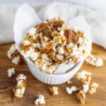 Sweet caramel popcorn with pecans in a white ramekin on a wooden surface, perfect for snack or party treat.