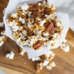 Crunchy caramel popcorn with pecans in a paper cone on a wooden surface.