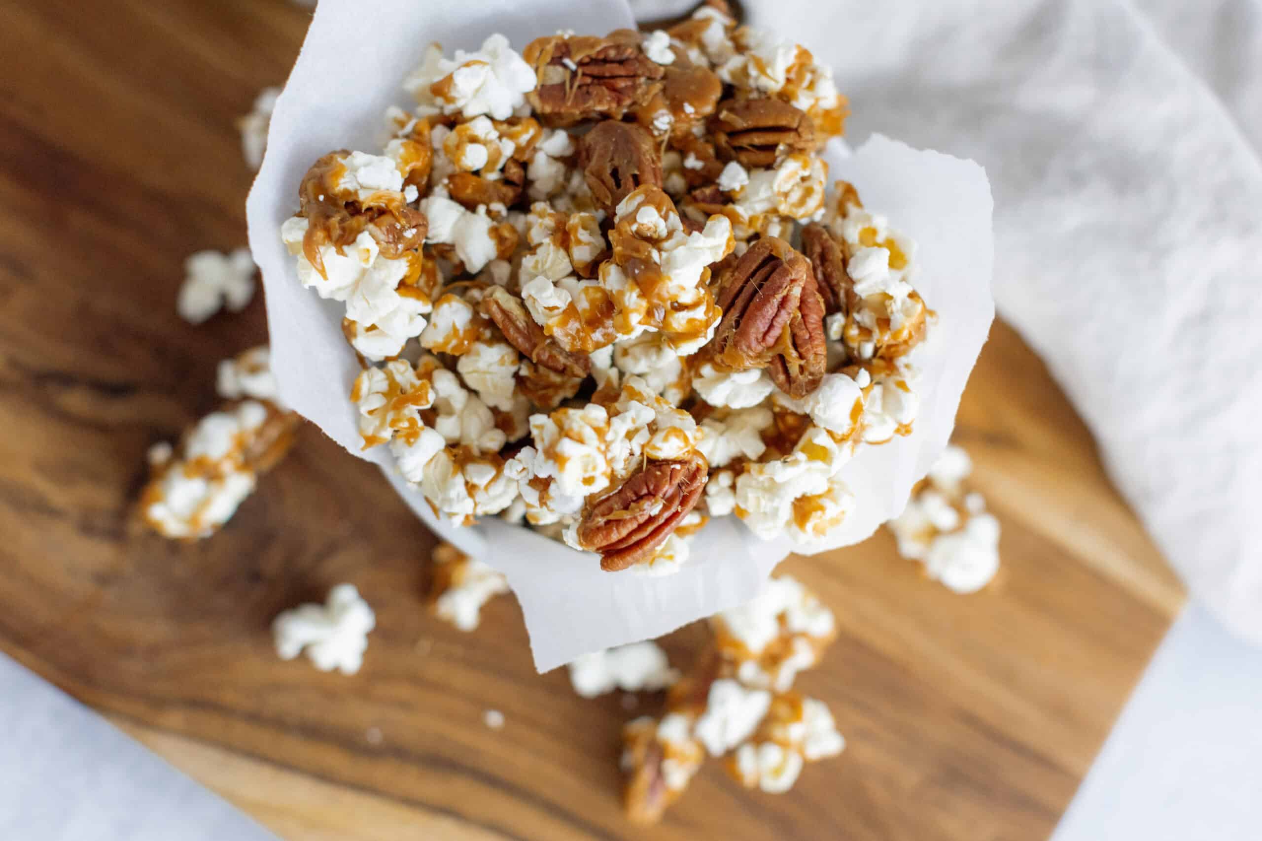 Crunchy caramel popcorn with pecans in a paper cone on a wooden surface.
