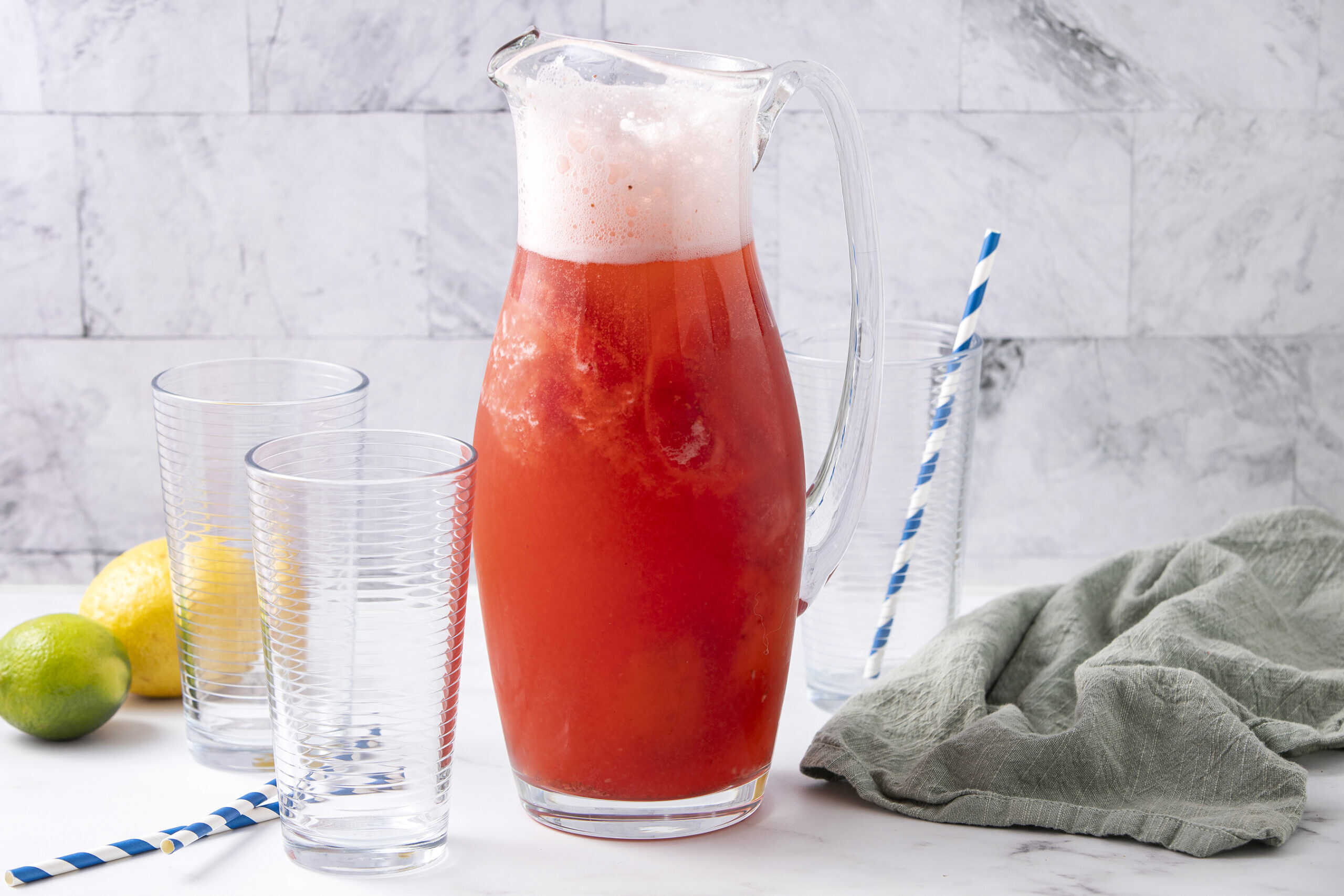 Refreshing watermelon lemonade pitcher with fresh fruit, clear glasses, and colorful straws on a bright kitchen counter.