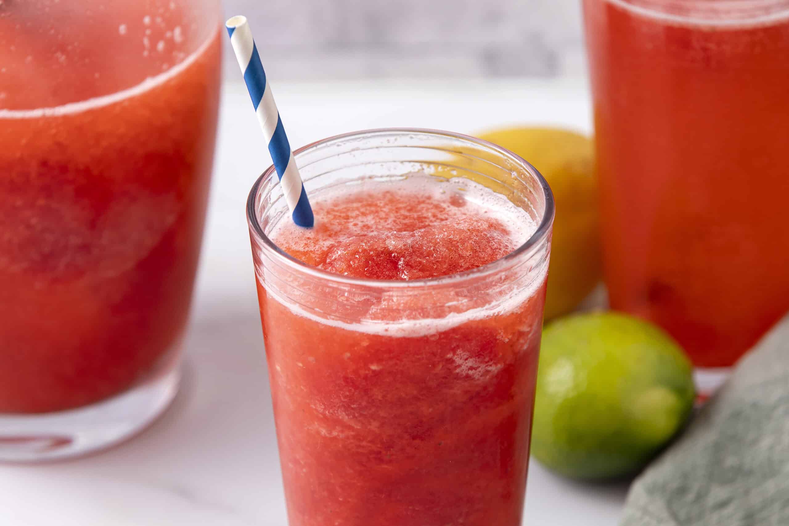 Refreshing strawberry limeade smoothie in a tall glass with a striped straw, featuring vibrant red color and frothy texture, perfect for summer drinks and fruit-based beverages.