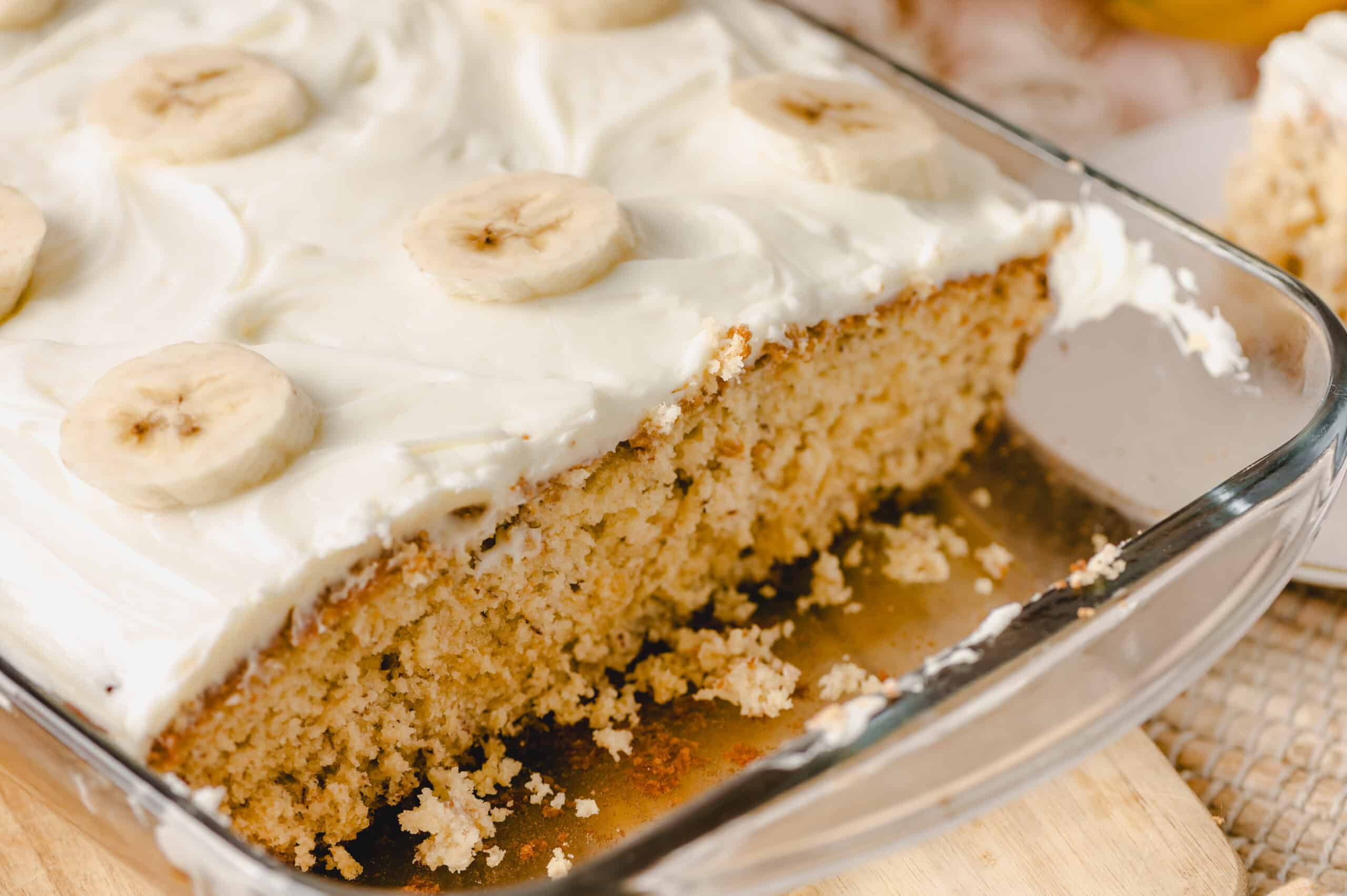 Banana cake with creamy frosting topped with sliced bananas in a glass baking dish. Perfect for banana dessert lovers and easy-to-make banana cake recipes.