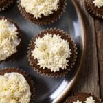 Cream cheese frosted chocolate cupcakes with white buttercream piping on top, served on a rustic wooden table.