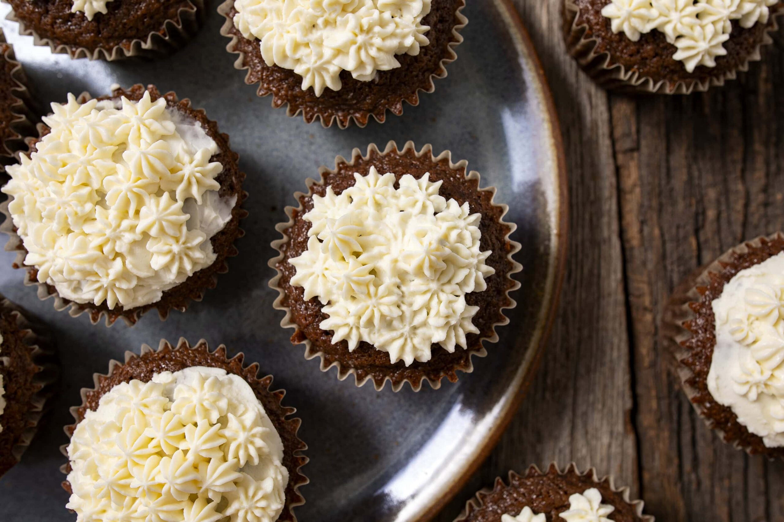 Cream cheese frosted chocolate cupcakes with white buttercream piping on top, served on a rustic wooden table.