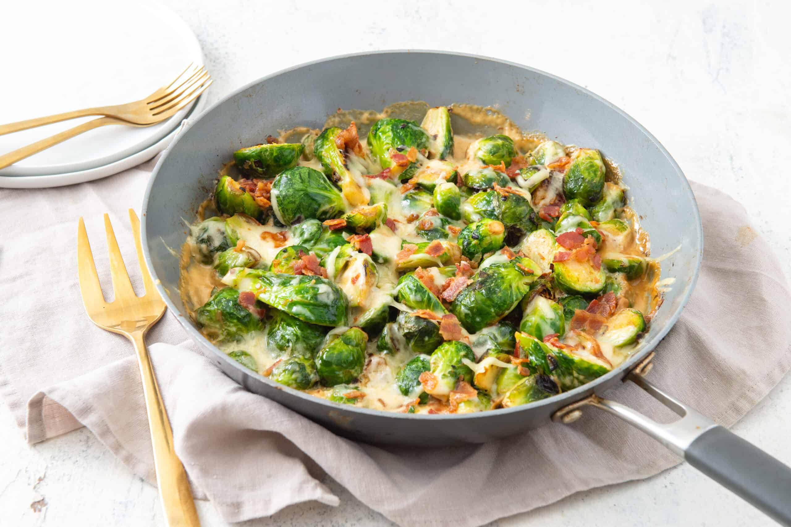 Sautéed Brussels sprouts with bacon and melted cheese in a skillet. Perfect for a savory side dish or healthy appetizer. Made with fresh ingredients and cooked to golden perfection. Ideal for dinner or party menus.