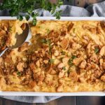Creamy chicken pot pie in a white ceramic baking dish with a flaky crust and seasoned chicken filling garnished with fresh parsley.