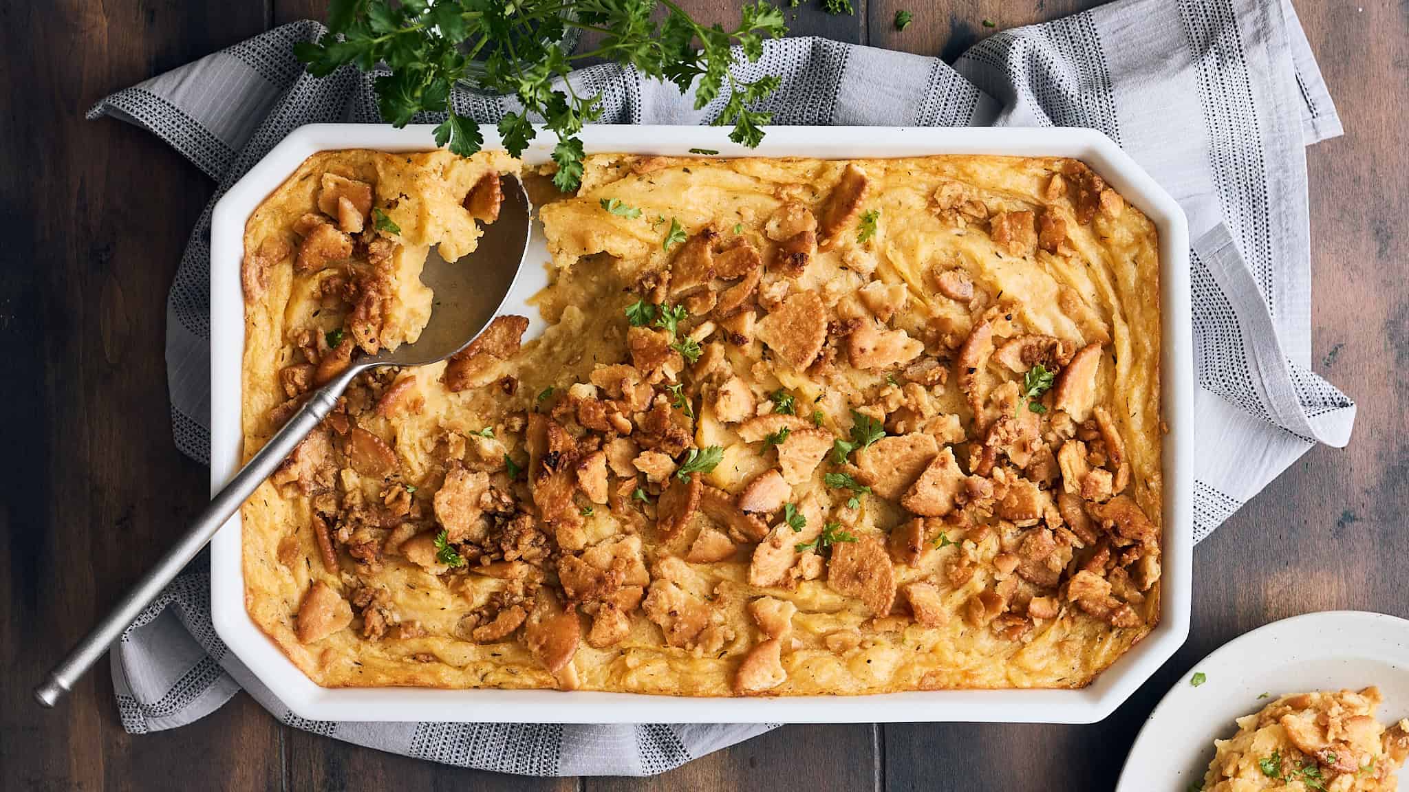 Creamy chicken pot pie in a white ceramic baking dish with a flaky crust and seasoned chicken filling garnished with fresh parsley.
