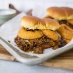 Savory cheeseburger sliders with melted cheese, crispy fried onion rings, and rich beef chili on soft slider buns on a baking sheet, served with dipping sauce and crunchy fries, perfect for parties and gatherings.