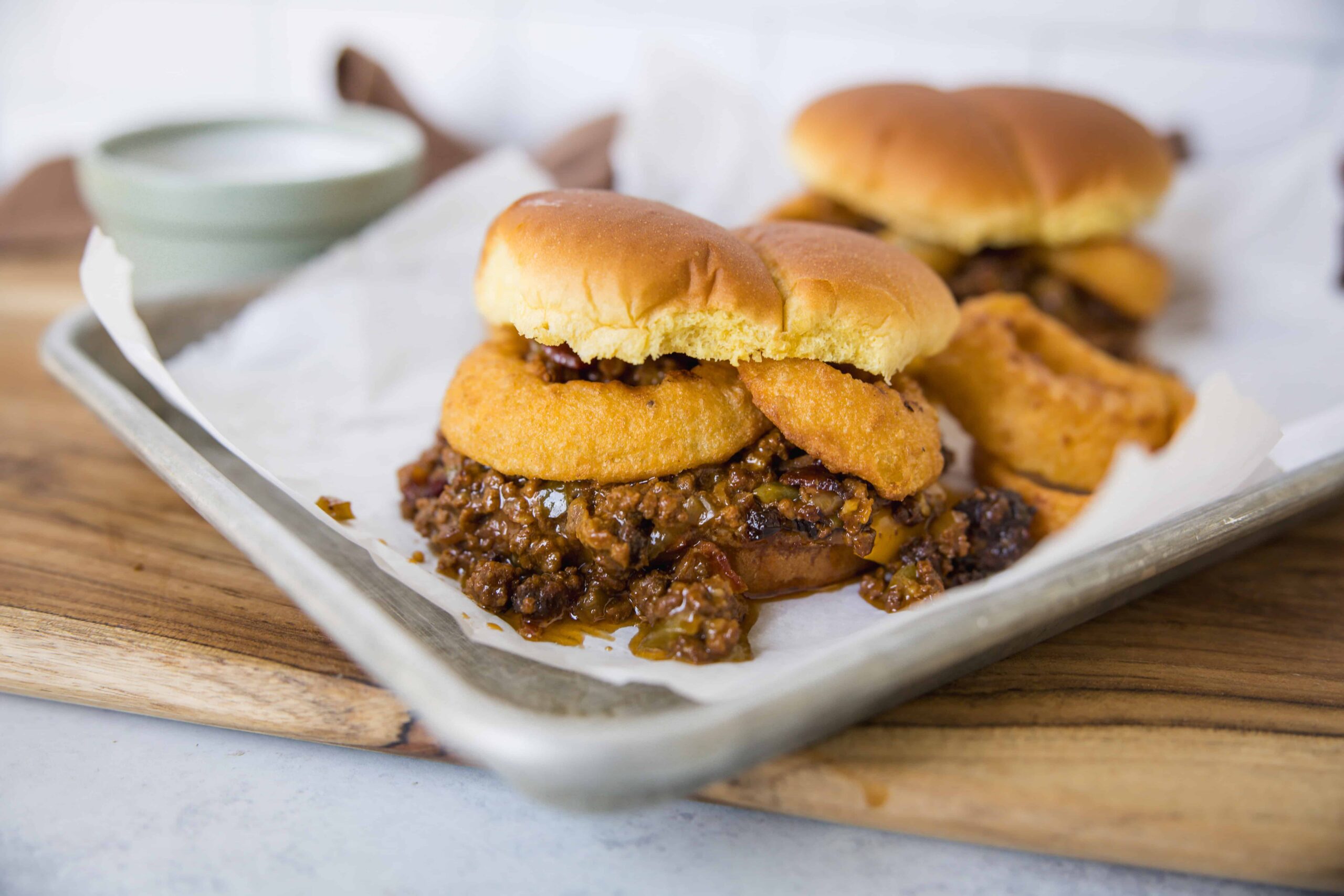 Savory cheeseburger sliders with melted cheese, crispy fried onion rings, and rich beef chili on soft slider buns on a baking sheet, served with dipping sauce and crunchy fries, perfect for parties and gatherings.