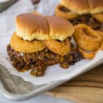 Crispy onion rings topped beef sliders with melted cheese on soft buns with caramelized onions on a tray with onion rings and ketchup, close-up, delicious fast food burger images, Hey Recipe, savory mini sandwiches, easy homemade meal, comfort food recipe.