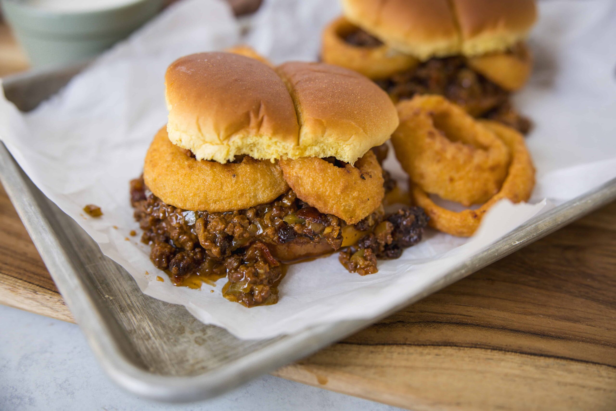 Crispy onion rings topped beef sliders with melted cheese on soft buns with caramelized onions on a tray with onion rings and ketchup, close-up, delicious fast food burger images, Hey Recipe, savory mini sandwiches, easy homemade meal, comfort food recipe.