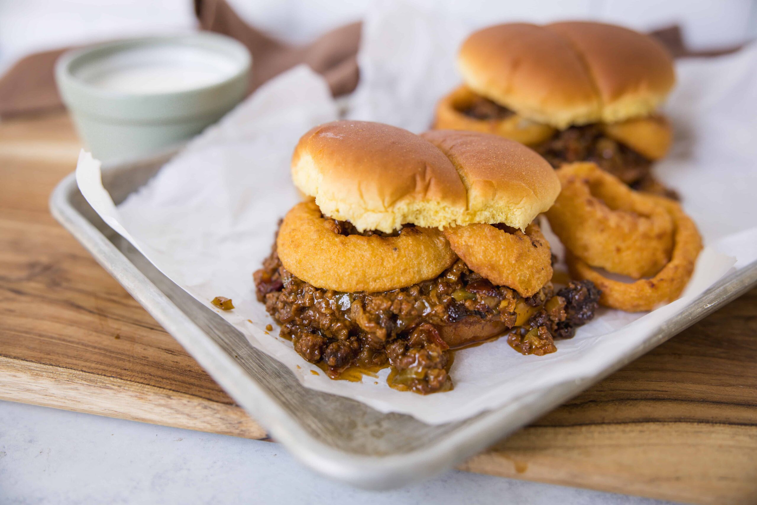 Savory sloppy joe sliders with onion rings on a white tray, served with dipping sauce, ready to enjoy classic comfort food.