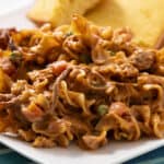 Creamy shredded chicken and vegetable filling with spices on a white plate served with cornbread, close-up.