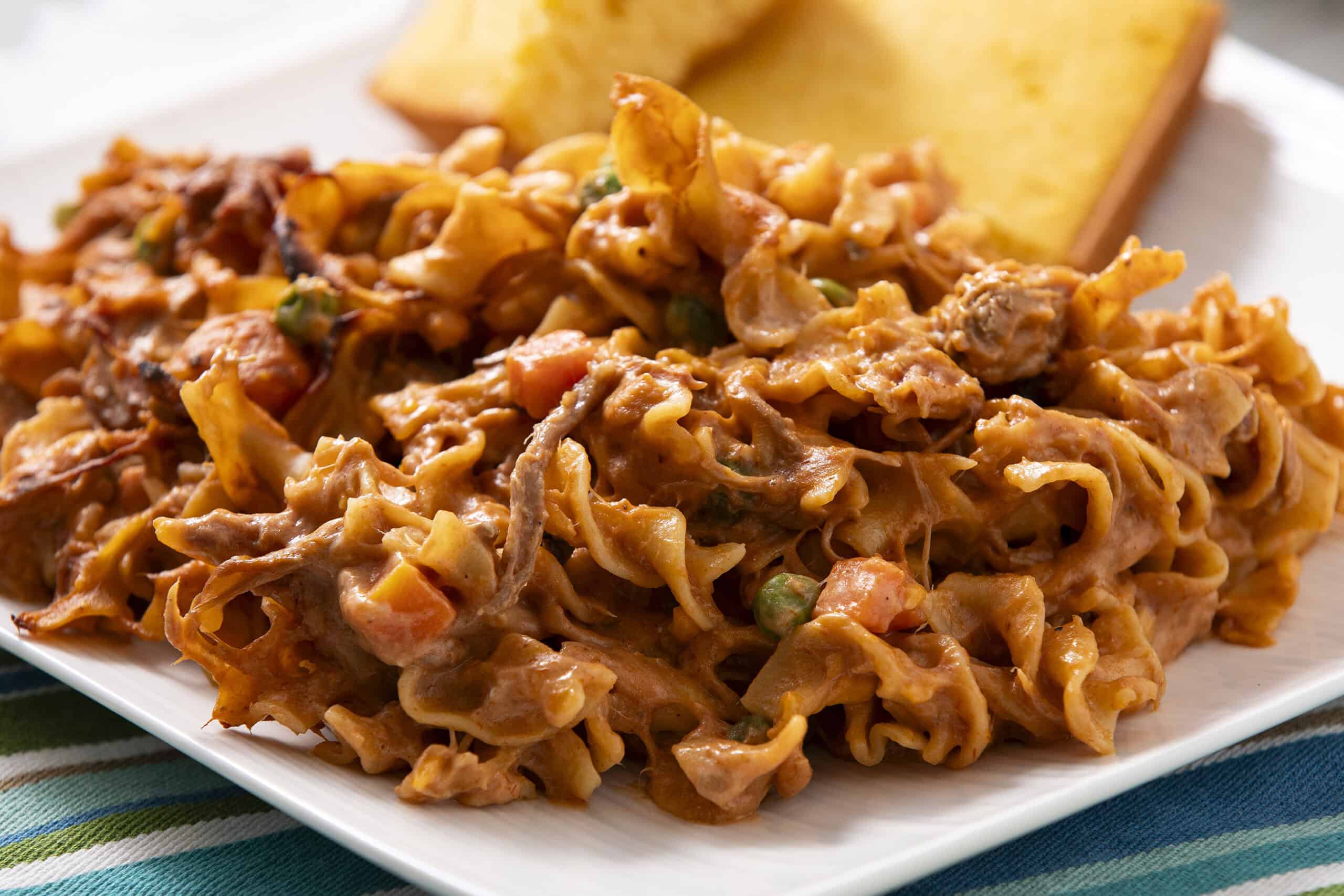 Creamy shredded chicken and vegetable filling with spices on a white plate served with cornbread, close-up.