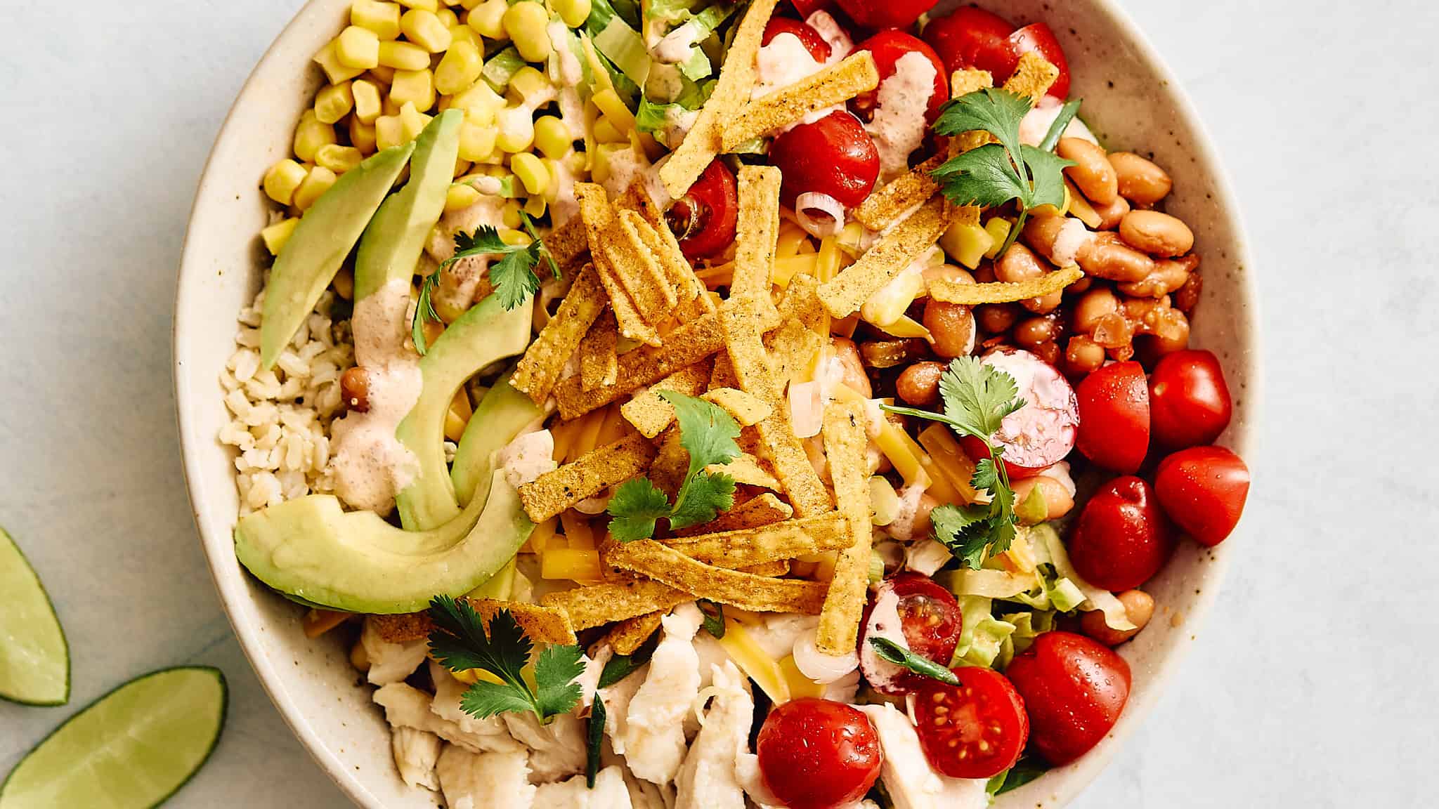 Fresh vegetable taco salad with cherry tomatoes, avocado, corn, beans, shredded chicken, crispy tortilla strips, and cilantro in a white bowl. Perfect healthy meal with colorful ingredients.