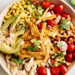 Fresh Mexican taco salad with beans, cherry tomatoes, avocado, shredded cheese, and crispy tortilla strips in a rustic bowl.
