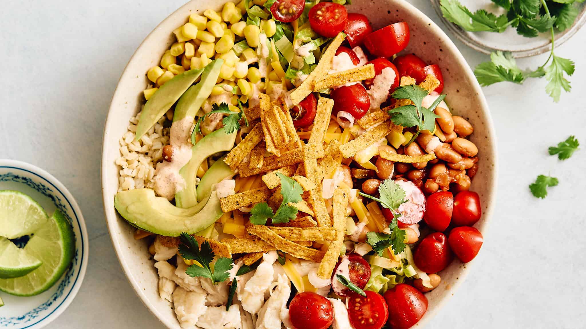 Fresh Mexican taco salad with beans, cherry tomatoes, avocado, shredded cheese, and crispy tortilla strips in a rustic bowl.