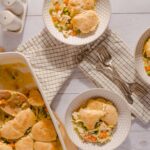 Creamy chicken pot pie with vegetables served in individual bowls, showcasing flaky crust and hearty filling, on a white wooden table.