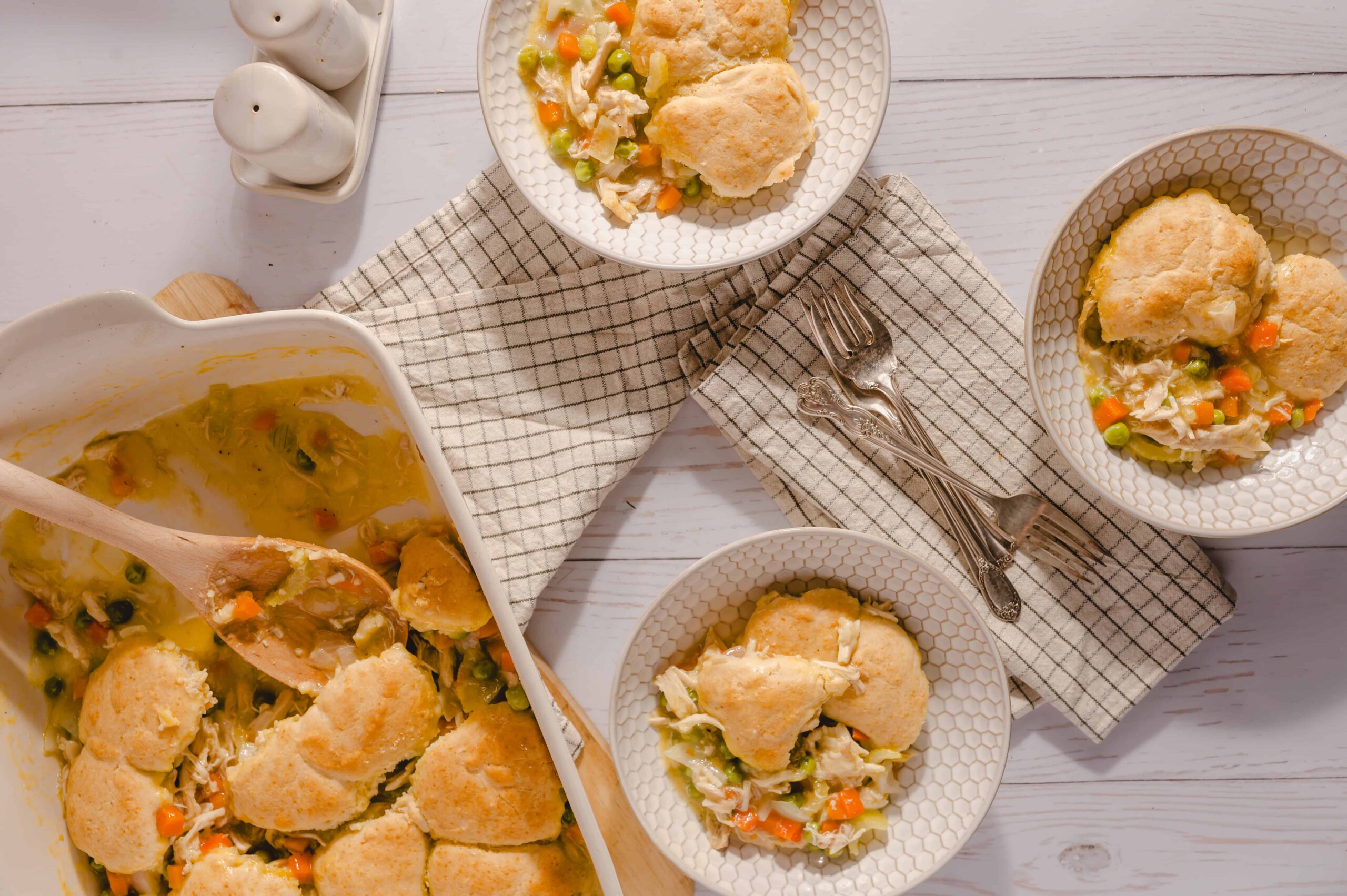 Creamy chicken pot pie with vegetables served in individual bowls, showcasing flaky crust and hearty filling, on a white wooden table.