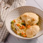 Fluffy homemade chicken pot pie with golden flaky crust served with mixed vegetables and gravy in a white patterned bowl.