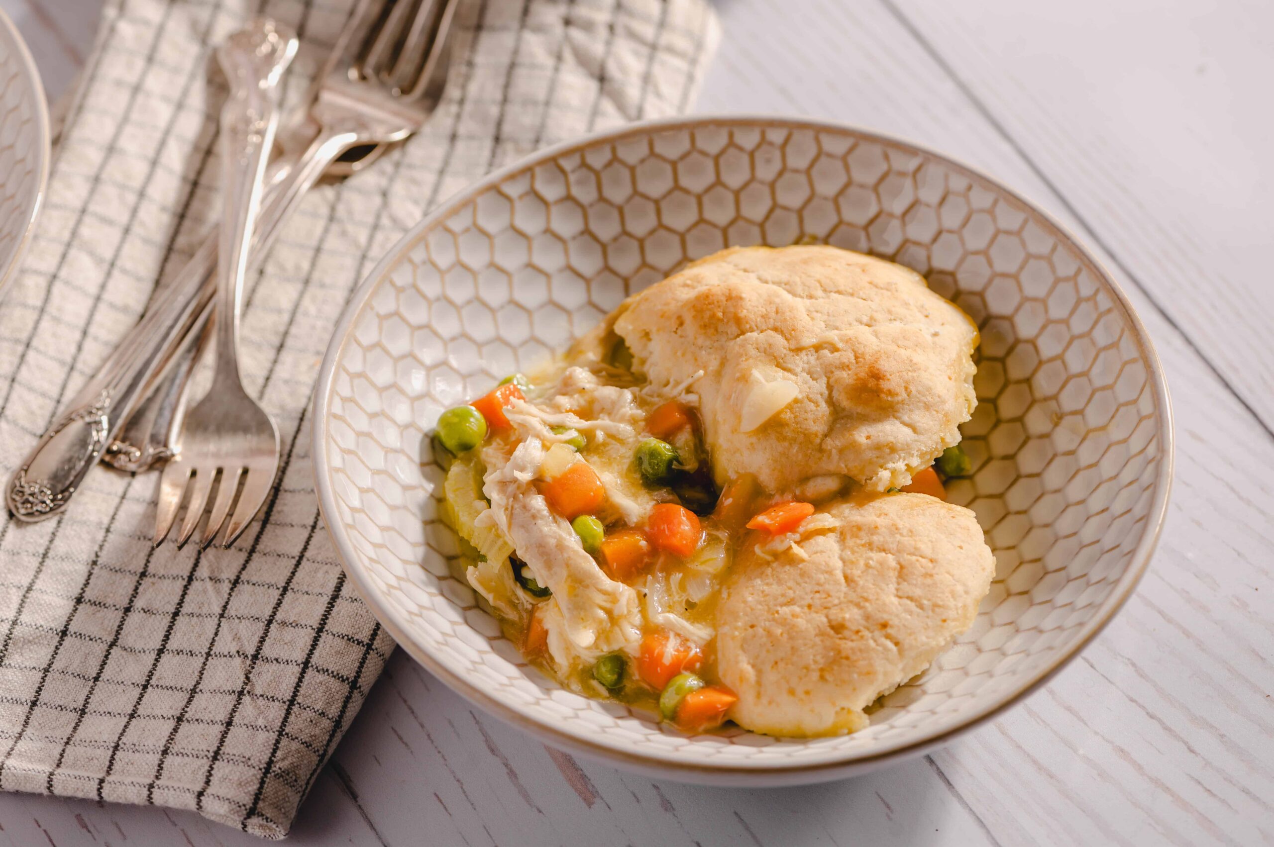 Fluffy homemade chicken pot pie with golden flaky crust served with mixed vegetables and gravy in a white patterned bowl.