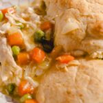 Creamy chicken pot pie with mixed vegetables and flaky golden crust, served hot in a white dish. Perfect comfort food for a cozy meal or family dinner.