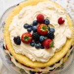 Fresh berry cake decorated with strawberries, blueberries, blackberries, and raspberries on a white ceramic plate for a sweet dessert or celebration.