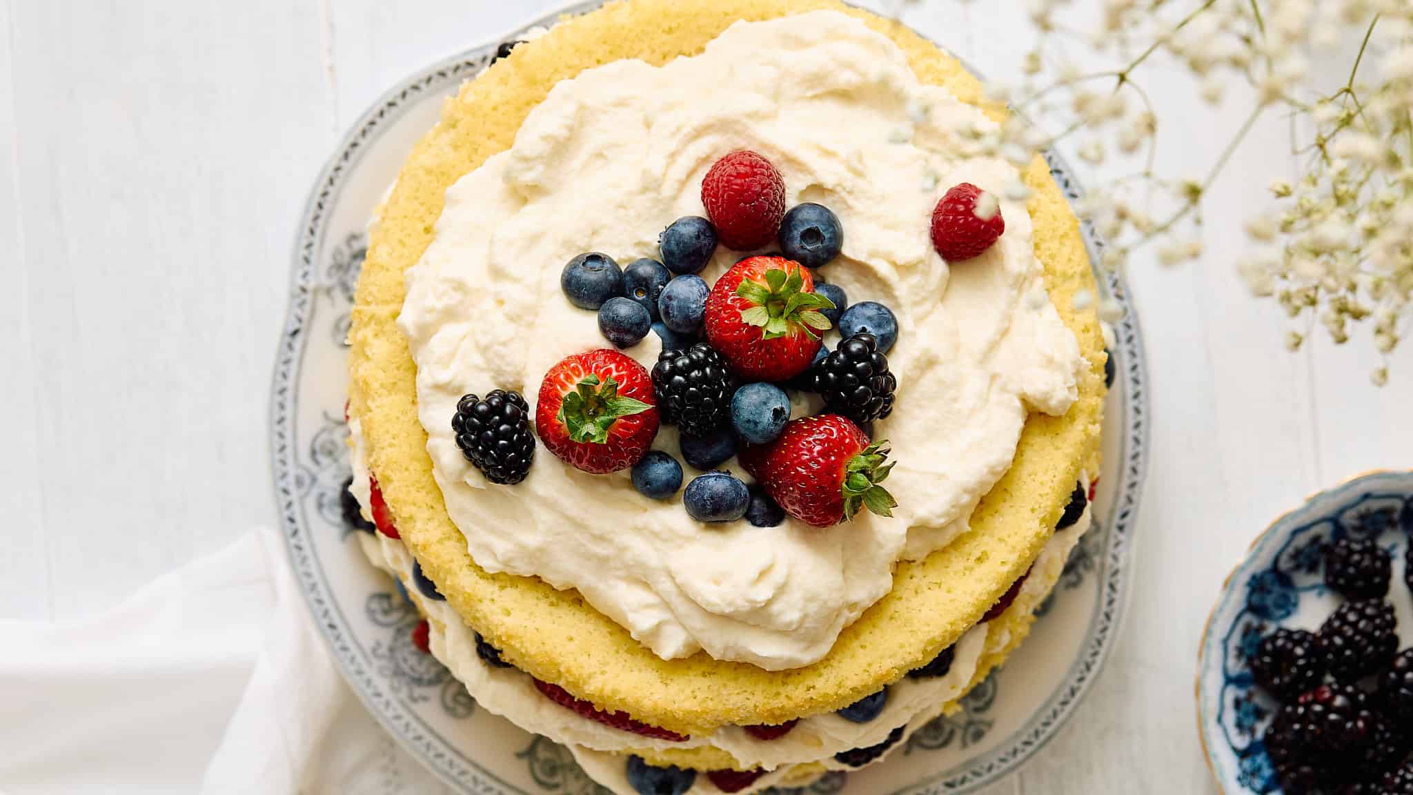 Fresh berry cake decorated with strawberries, blueberries, blackberries, and raspberries on a white ceramic plate for a sweet dessert or celebration.