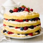 Fresh berry shortcake with layers of sponge cake, whipped cream, and assorted berries on a decorative platter. Perfect for summer desserts and berry recipes.