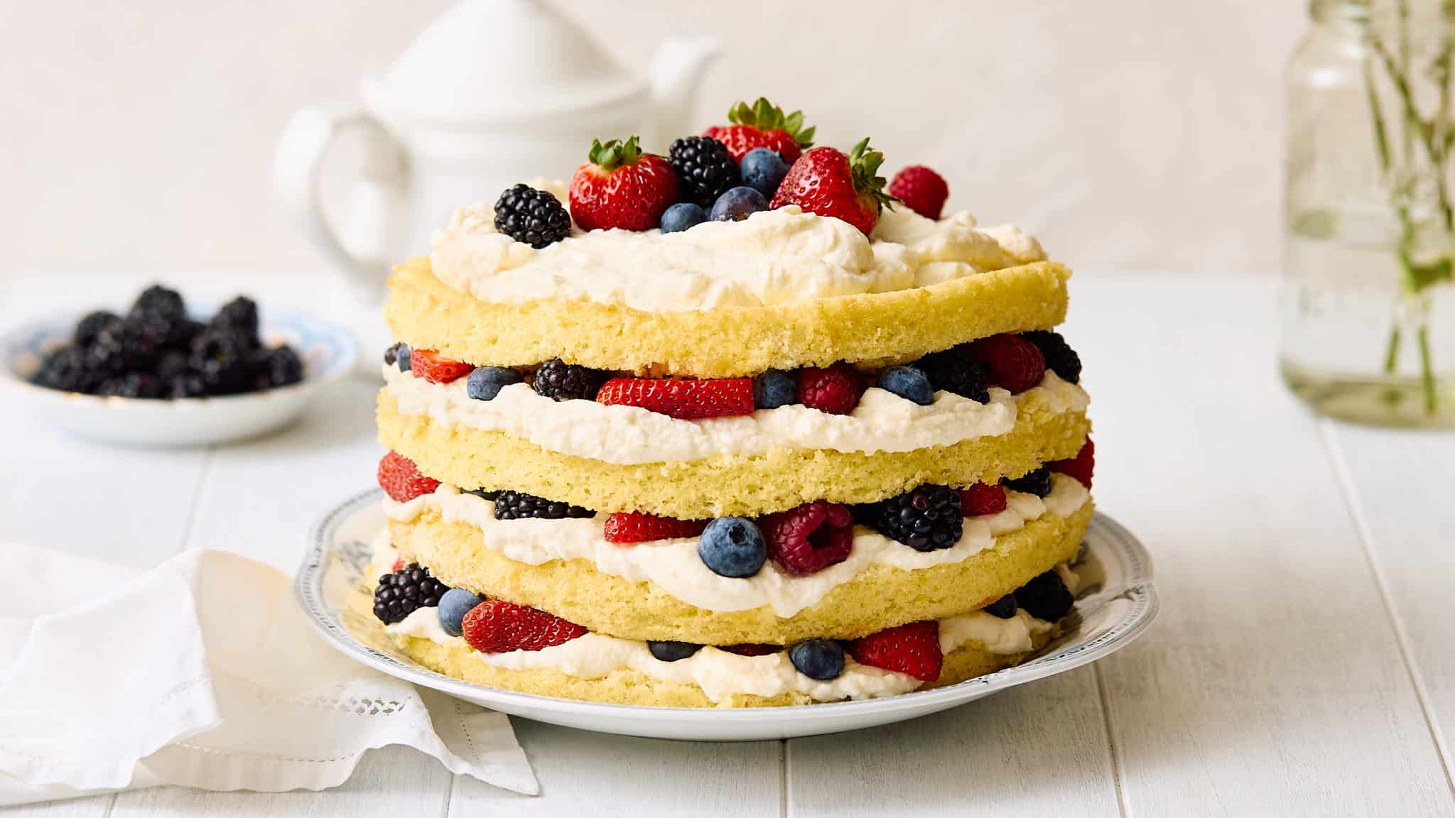 Fresh berry shortcake with layers of sponge cake, whipped cream, and assorted berries on a decorative platter. Perfect for summer desserts and berry recipes.