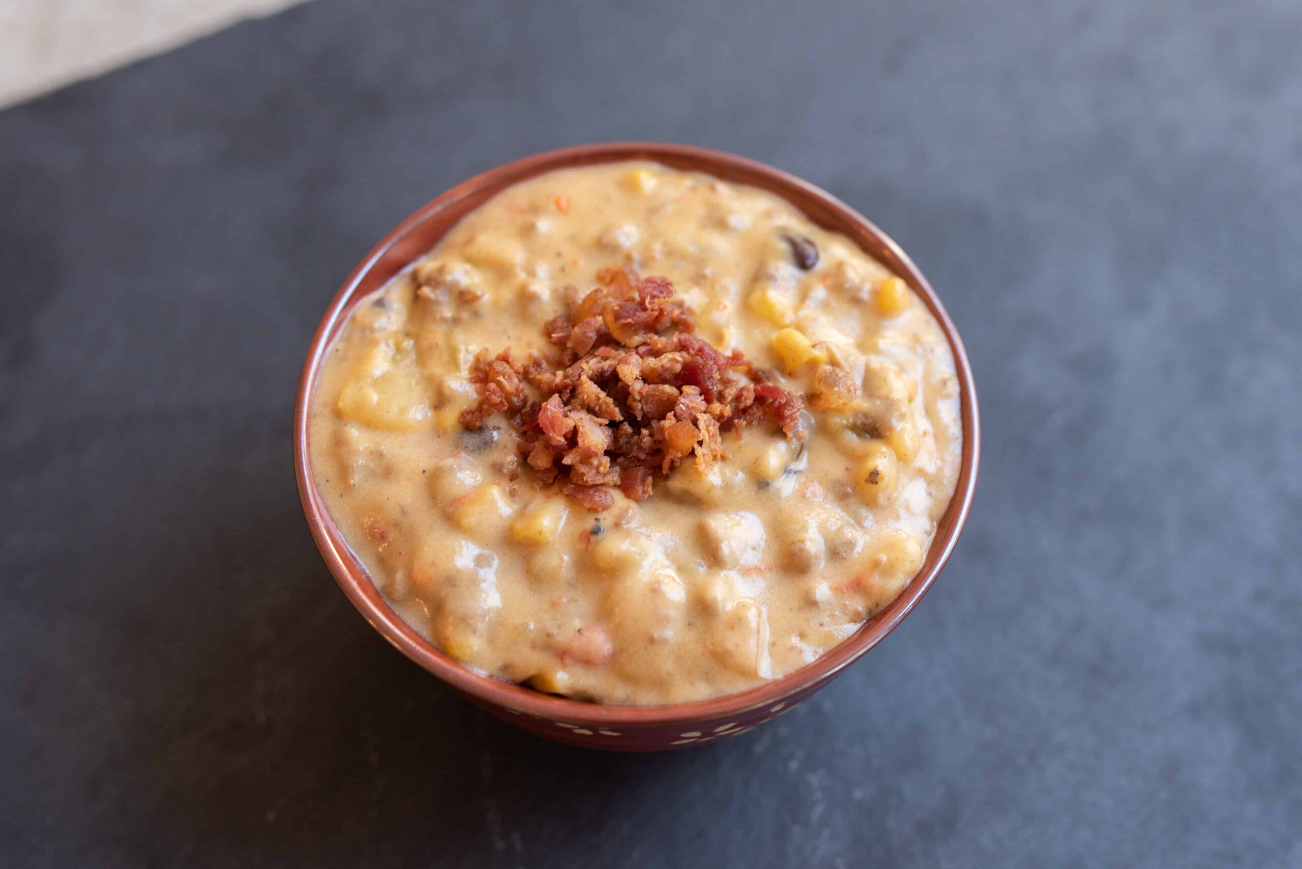 Creamy corn and bacon chowder in a ceramic bowl, topped with crispy bacon bits, served on a dark surface. Perfect comfort food recipe for cold days and sweet corn lovers at Hey Recipe.